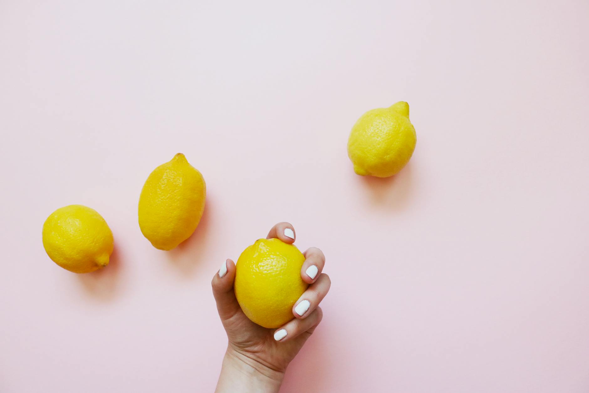 Hand holding a fresh lemon against a soft pink background, symbolizing slow, intentional healing