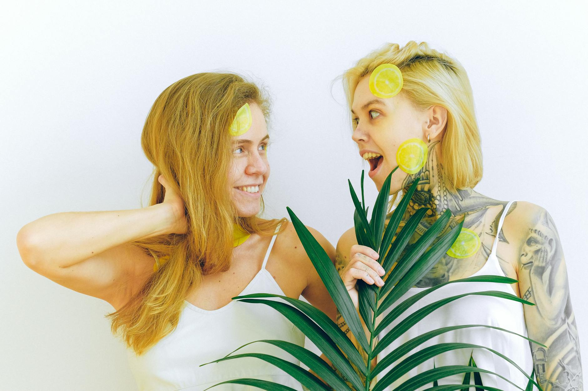 Two women smiling with lemons and tropical plants, expressing joy and vitality