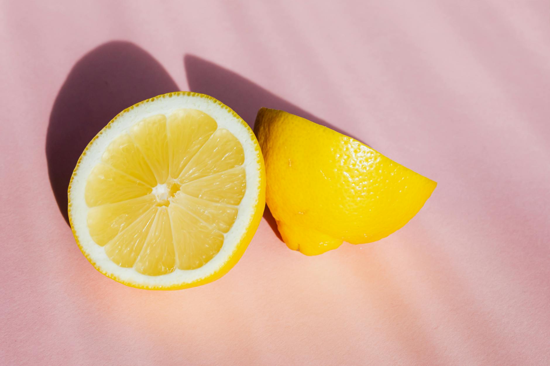 Fresh lemon halves on a pink background with natural light, symbolizing citrus-inspired pleasure and sensitivity