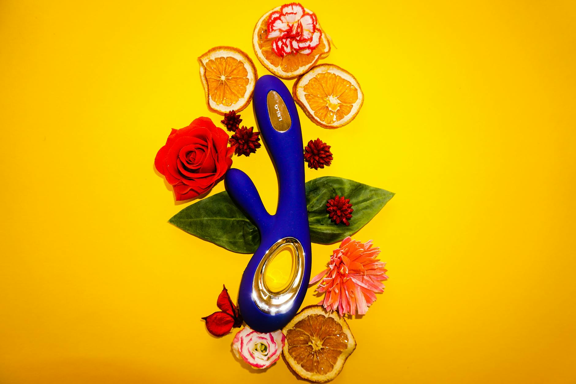 A bright yellow lemon vibrator surrounded by fresh flowers on a warm yellow background.