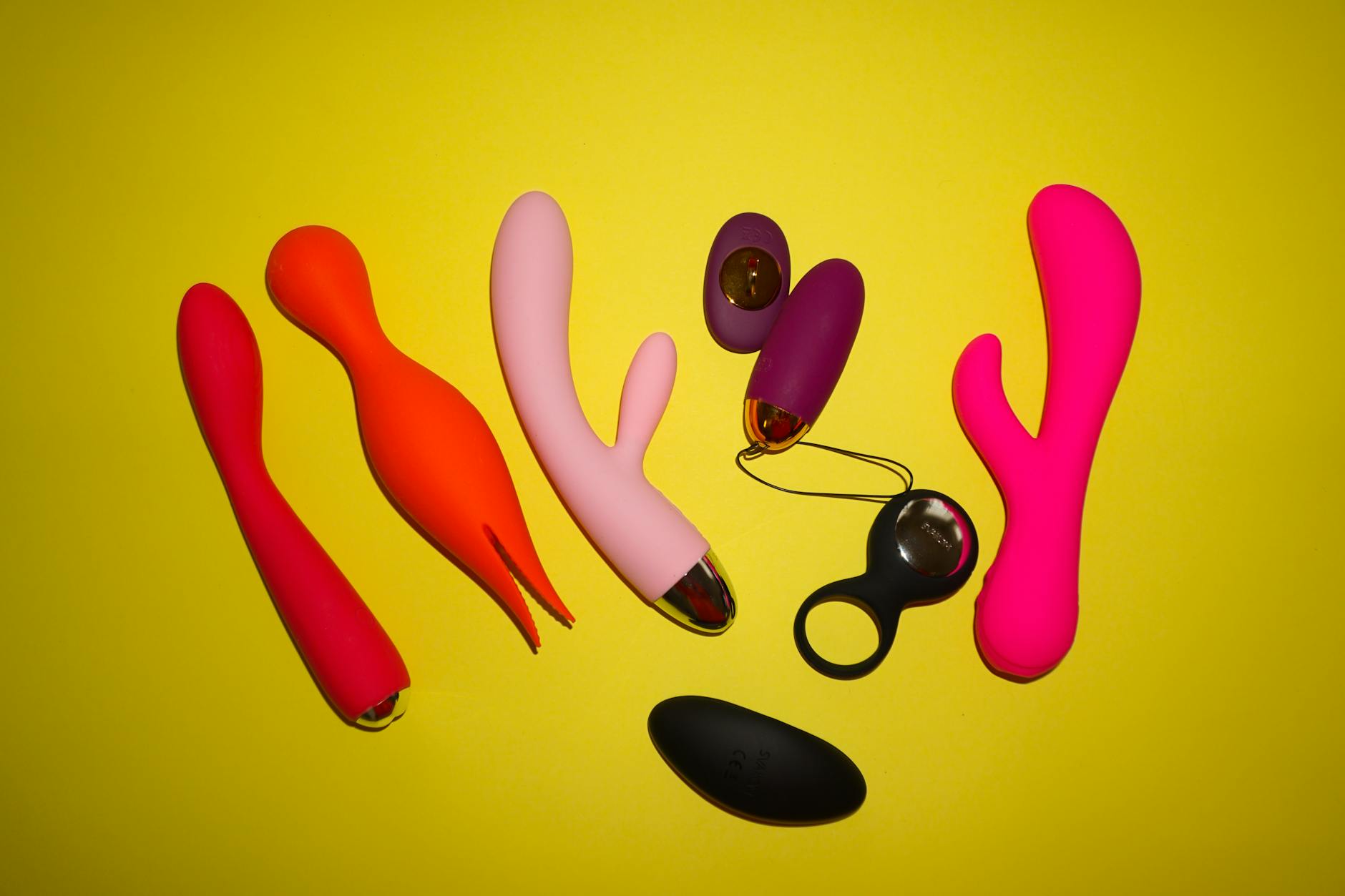 Close-up of colorful clitoral vibrators and adult toys on a bright yellow background
